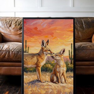 May include: A framed oil painting featuring two foxes in a desert landscape at sunset. The scene depicts one fox standing and one sitting on rocky ground, surrounded by saguaro cacti. The sky is painted in vibrant shades of orange, pink, and yellow.