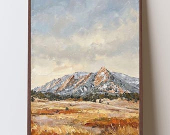 May include: A vertical oil painting in a dark brown frame depicting a mountain range with snow-dusted peaks under a pale blue sky. The foreground features a textured landscape of golden, orange, and brown grasses and shrubs in a field.