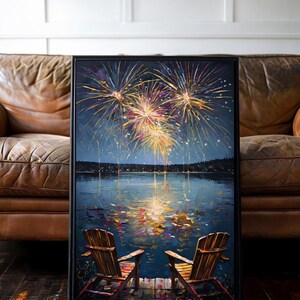 May include: A framed painting depicting two wooden chairs on a dock overlooking a dark lake at night. Above the horizon, vibrant yellow, orange, and purple fireworks explode in the sky, with their colorful reflections shimmering on the water surface.