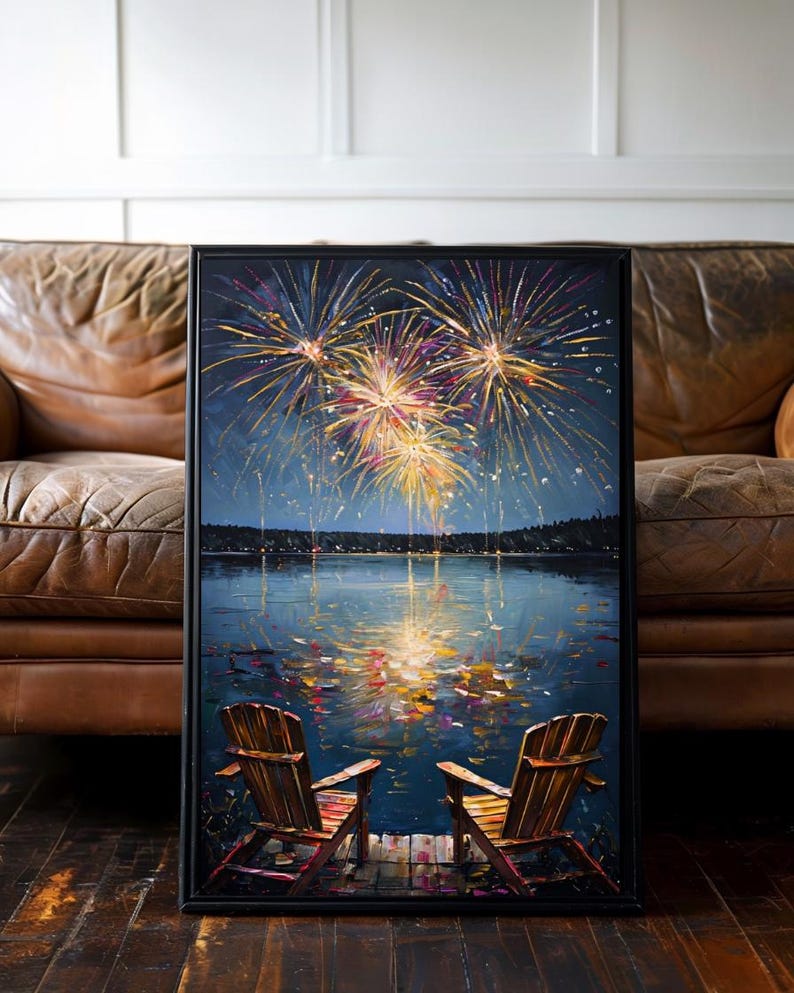 May include: A framed painting depicting two wooden chairs on a dock overlooking a dark lake at night. Above the horizon, vibrant yellow, orange, and purple fireworks explode in the sky, with their colorful reflections shimmering on the water surface.