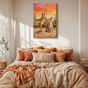May include: A rectangular wall art print featuring an oil painting of two foxes in a desert landscape at sunset. The scene depicts one fox standing and one sitting on sandy ground, with tall cacti in the background under a vibrant orange sky.