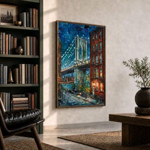 May include: A framed painting of the Brooklyn Bridge at night, with illuminated lights and a cityscape in the background. The artwork features a dark blue sky, a bridge with lights, and buildings with red brick facades. The painting is displayed in a room with a bookshelf and a leather chair.