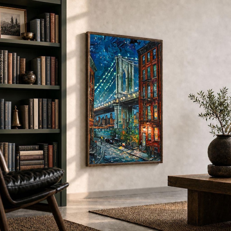 May include: A framed painting of the Brooklyn Bridge at night, with illuminated lights and a cityscape in the background. The artwork features a dark blue sky, a bridge with lights, and buildings with red brick facades. The painting is displayed in a room with a bookshelf and a leather chair.