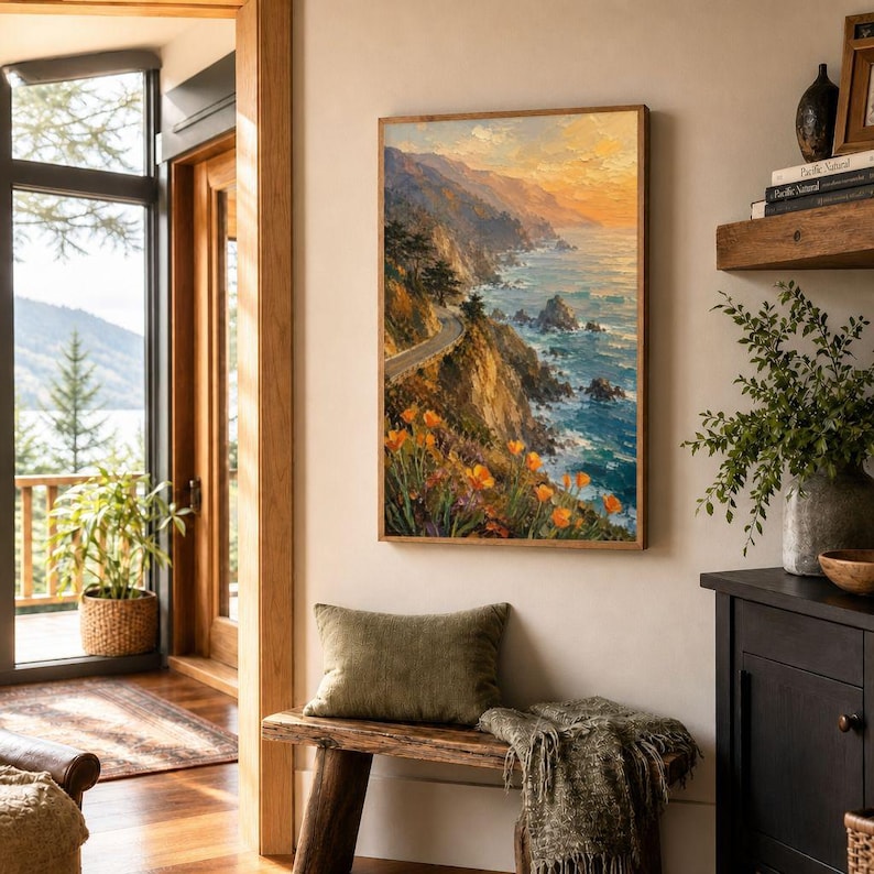 May include: A framed landscape painting depicts a coastal scene with a winding road, cliffs, and ocean. The artwork features vibrant colors, including orange flowers, blue water, and a sunset sky. The painting is displayed in a room with a wooden bench and a green pillow.