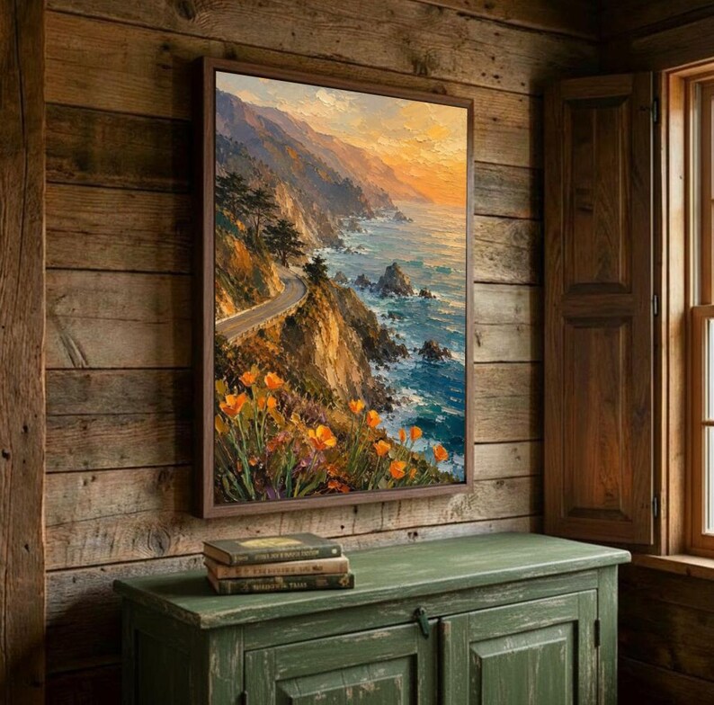 May include: A framed landscape painting depicts a coastal scene with a winding road along a cliffside. The artwork features vibrant colors, including orange flowers, blue ocean, and a warm sunset. The painting is displayed on a wooden wall above a green cabinet.