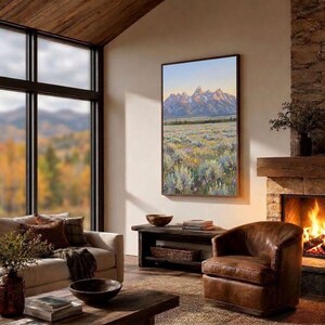 May include: A vertical rectangular wall art print depicting a mountain range with snow-capped peaks rising above a vast field of sagebrush and wildflowers. The painting features soft morning light, muted green tones, and purple floral accents.