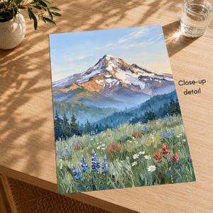 Pu&ograve; includere: Una stampa artistica rettangolare che raffigura un dipinto a olio di una vetta innevata che si erge sopra una fitta foresta e un prato vivace pieno di lupini blu, castilleja rosse e margherite bianche sotto un cielo azzurro tenue.