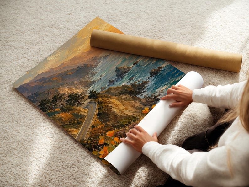 May include: An oil painting of a coastal landscape with a winding road, in shades of orange, blue, and brown. A rolled-up canvas and a brown cardboard tube are next to the painting. The painting is on a white surface.
