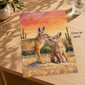 May include: An oil painting print featuring two foxes in a desert landscape with saguaro cacti under a vibrant orange and pink sunset sky. The artwork displays thick, textured brushstrokes and includes the text Close-up detail on the right.