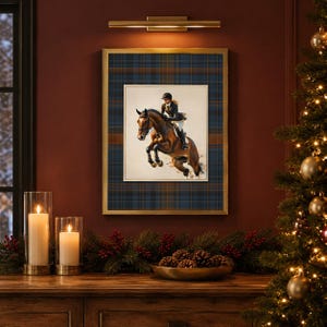 May include: A framed wall art print featuring a brown horse jumping with a rider in equestrian gear. The artwork is set against a dark blue and brown plaid background within a gold frame, displayed on a wall with a light fixture above it.
