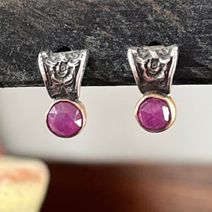 May include: A pair of silver earrings with a floral design and a ruby gemstone in the center of each earring.