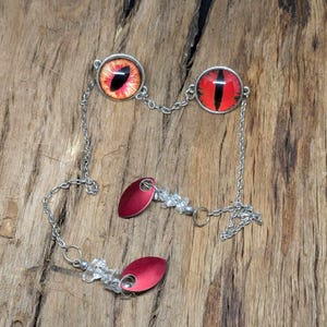 May include: A silver chain necklace with two red eye charms and two red metal charms with clear crystal accents.