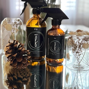 May include: Two amber glass spray bottles with black spray tops and labels. The labels are black with white text and a green circle with a white letter "f" inside. The text on the labels reads "Fili" and "φιλί".