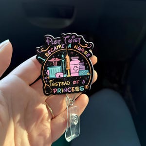 May include: A black badge reel with the text "I BECAME A NURSE INSTEAD OF A PRINCESS." The badge features medical-themed illustrations in teal, pink, and yellow. The reel has a clear plastic clip and a retractable cord.