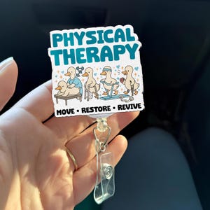 May include: A white badge with the words "PHYSICAL THERAPY" in teal. The badge features cartoon ducks in various physical therapy scenarios. The words "MOVE • RESTORE • REVIVE" are below the ducks. The badge is attached to a retractable reel.