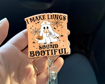 Peut inclure: Un porte-badge sur le thème d'Halloween avec le texte "I MAKE LUNGS SOUND BOOTIFUL". Le badge représente un fantôme portant une coiffe d'infirmière et tenant un stéthoscope. Fond orange avec des toiles d'araignées et une citrouille.