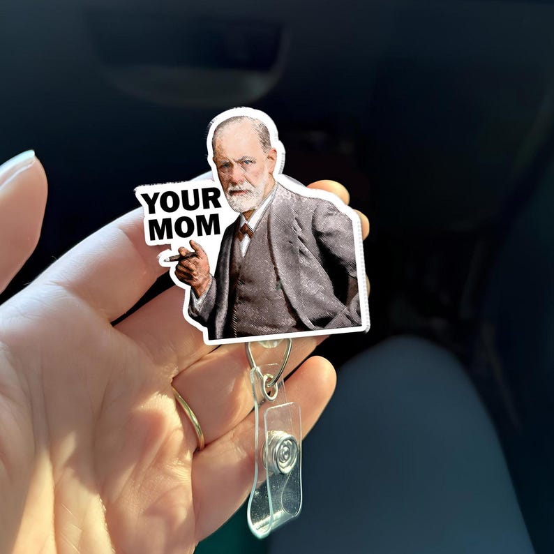 Puede incluir: Una pegatina blanca con un retrato de un hombre con traje, sosteniendo un cigarro, con el texto "YOUR MOM". La pegatina est&aacute; adherida a un portatarjetas de pl&aacute;stico transparente con un clip met&aacute;lico.