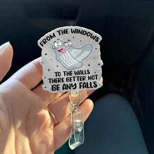 May include: A badge reel with a cartoon image of two socks with faces and the text "FROM THE WINDOWS TO THE WALLS THERE BETTER NOT BE ANY FALLS". The badge reel has a clear plastic clip and a silver-colored metal ring.