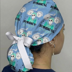 May include: A light blue surgical scrub cap with a white bow. The cap features a repeating pattern of a skeleton in surgical attire, surgical lights, and the words "SURGICAL Gangsta" in black and teal.