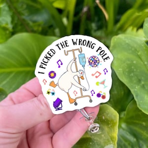 May include: A white badge reel with the text "I PICKED THE WRONG POLE" and a cartoon goose hanging from an IV pole. The design includes musical notes, a disco ball, and a cocktail.