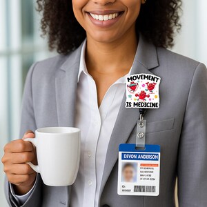 May include: A white badge with the text "MOVEMENT IS MEDICINE" and cartoon hearts. Below, a blue and white ID card with the name "DEVON ANDERSON" is visible. The person is wearing a gray blazer and holding a white mug.