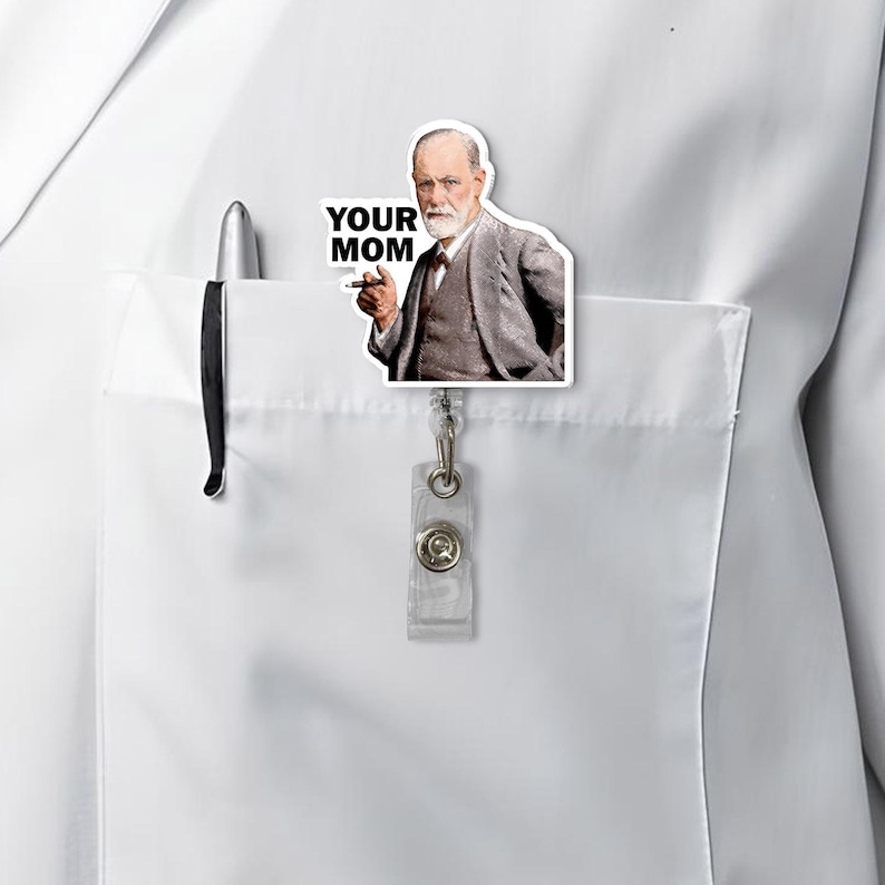 Puede incluir: Un portatarjetas blanco con una imagen de Sigmund Freud con el texto "YOUR MOM". El portatarjetas est&aacute; sujeto a un bolsillo de camisa blanco, junto a un bol&iacute;grafo.