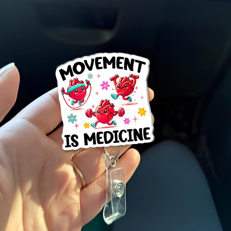 May include: A white badge reel with the words "MOVEMENT IS MEDICINE" and cartoon hearts exercising. The hearts are red with smiling faces and are shown jumping rope, running, and lifting weights. The reel has a clear plastic ID holder.