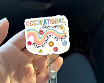 Puede incluir: Un portatarjetas con el texto "OCCUPATIONAL therapy" sobre un diseño de arcoíris y las palabras "EVERY MILESTONE MATTERS". El portatarjetas tiene un clip de plástico transparente y un cordón retráctil de metal.
