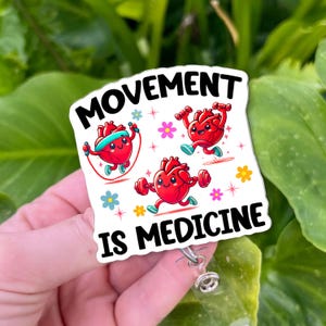 May include: A white badge reel with the text "MOVEMENT IS MEDICINE" and illustrations of cartoon hearts exercising. One heart jumps rope, another runs, and the third lifts weights. Colorful flowers surround the hearts.