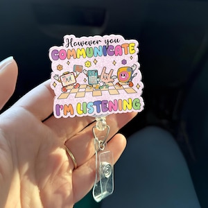 May include: A badge reel with a colorful design and the text "However you COMMUNICATE I'M LISTENING". The design features cartoon characters and a checkered floor pattern. The reel has a clear plastic holder and a metal clip.