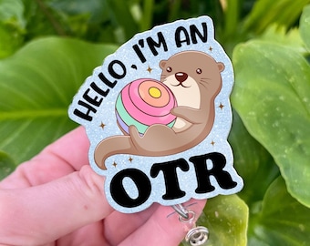 May include: A badge reel with a cartoon otter holding a colorful ball. The badge has the text "HELLO, I'M AN OTR" in black letters on a light blue background with small star accents. The reel has a clear plastic strap and a metal clip.