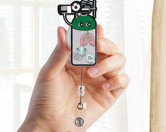 Pode incluir: Um porta-crachá retrátil com um personagem de cilindro de oxigênio de desenho animado com rosto sorridente, pulmões rosa, uma máscara de oxigênio verde e um rótulo O2. O cilindro tem um manômetro preto e uma alça de plástico transparente.