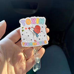 May include: A badge reel with the words "TOXIN TERMINATOR" in colorful bubble letters. The design features a cartoon kidney kicking, with a blue scarf and white karate uniform. The background is glittery.
