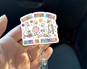 Könnte beinhalten: Ein Ausweis-Rollhalter mit einem farbenfrohen Design mit Cartoon-Gänsen in verschiedenen Posen, mit dem Text "SMALL STEPS STILL MOVE US FORWARD". Die Gänse sind mit Trainingsgeräten und medizinischem Zubehör dargestellt.