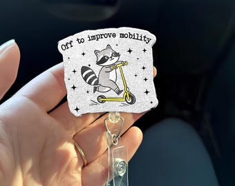 May include: A white and gray badge reel with a cartoon raccoon riding a yellow scooter. The text "Off to improve mobility" is printed on the badge. The badge reel has a clear plastic holder and a metal clip.