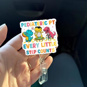 Puede incluir: Un portatarjetas colorido con tres dinosaurios de dibujos animados. El texto "Pediatric PT" y "Every Little Step Counts" están en la imagen. El portatarjetas tiene un soporte de plástico transparente y un cordón retráctil.