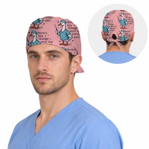Pu&ograve; includere: Una cuffia chirurgica rosa con un motivo ripetuto di un'anatra dei cartoni animati che indossa una casacca e una cuffia chirurgica color verde acqua, mentre tiene in mano un bisturi. Il testo recita, Here's the thingy with the pointy end.