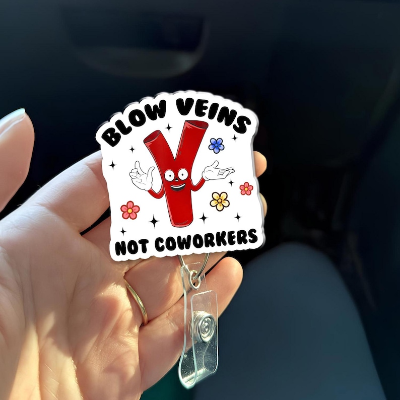 May include: A white badge reel with the text "BLOW VEINS NOT COWORKERS" and a cartoon vein character. The vein is red with a smiling face and arms. The badge reel has a clear plastic clip and a retractable cord.