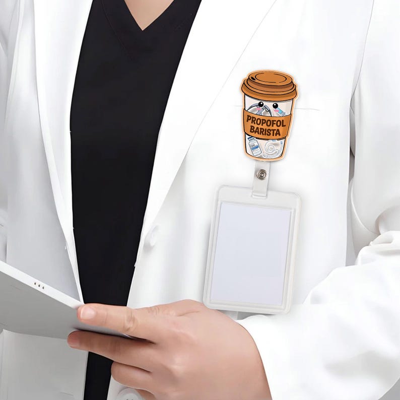 May include: A coffee cup-shaped badge reel with the text "PROPOFOL BARISTA" and cartoon syringes and vials. The badge reel is attached to a white lanyard and a white ID badge holder. The image is set against a white lab coat.