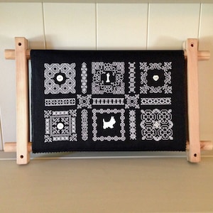 May include: Black embroidery hoop with a white design of various geometric shapes and a small dog silhouette. The hoop is made of wood and has a natural finish.