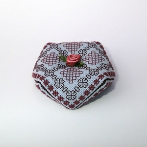 May include: A small, heart-shaped pincushion with a blue and white geometric pattern and a pink rose on top.
