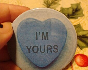 May include: A blue heart-shaped button with the text "I'm Yours" on it. The button is on a floral background.