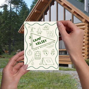 two hands holding the printed invitation up, with a cabin in the background