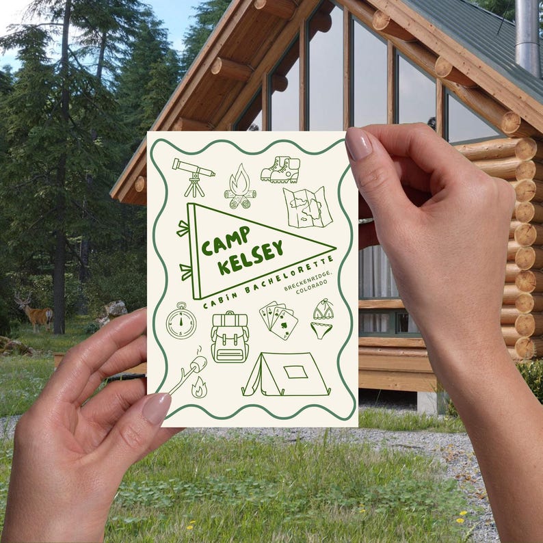 two hands holding the printed invitation up, with a cabin in the background