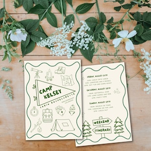 An aesthetic photo of the invitation printed out. It shows the front and back laying on a wood table, surrounded by greenery