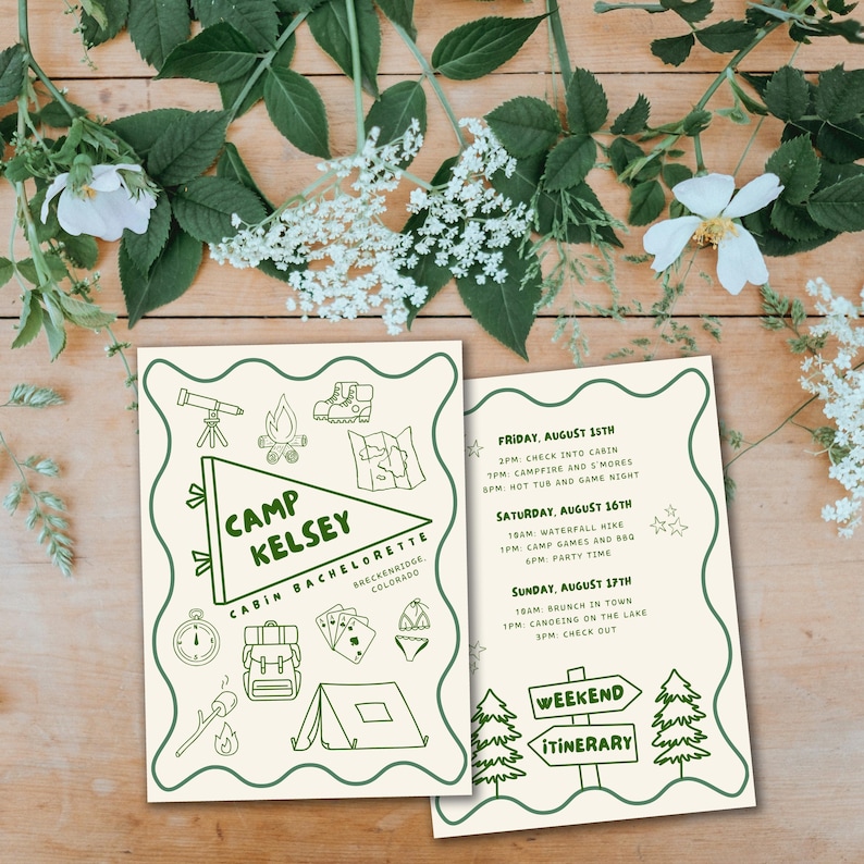 An aesthetic photo of the invitation printed out. It shows the front and back laying on a wood table, surrounded by greenery
