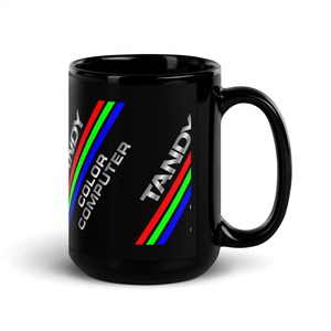Könnte beinhalten: Schwarze Keramiktasse mit einem Tandy Color Computer Logo. Das Logo zeigt ein diagonales Streifenmuster in Rot, Grün und Blau.