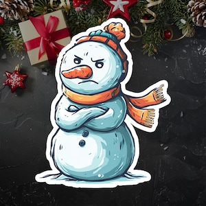 May include: A cartoon illustration of an angry snowman with a carrot nose, wearing an orange scarf and hat. The snowman has crossed arms and a grumpy expression. The image has a white border and is likely a sticker or decal.