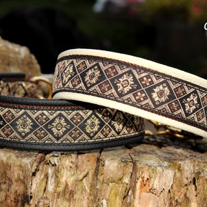 Puede incluir: Dos collares para perros con base de cuero negro y ribete con estampado marr&oacute;n y dorado. Los collares est&aacute;n sobre una superficie de madera.