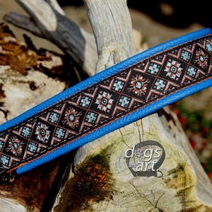 May include: A blue leather dog collar with a black and brown patterned fabric insert. The collar has a silver D-ring.